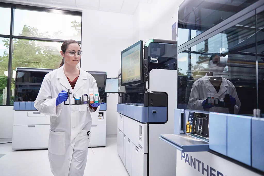 Auxiliar de laboratorio que lleva una bandeja de muestras para cargarla en el sistema Panther