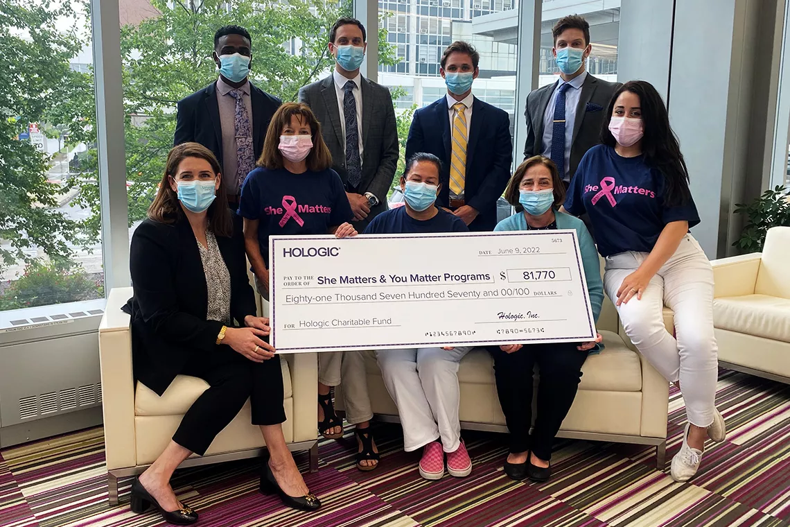 Fotografía de un grupo de personas con mascarilla sosteniendo un gran cheque promocional para los programas She Matters y You Matter