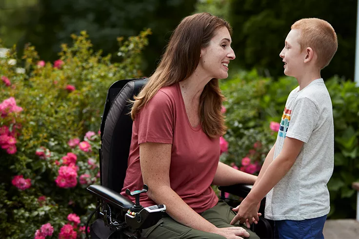 Mujer en silla de ruedas sonriendo junto a un niño en una zona exterior